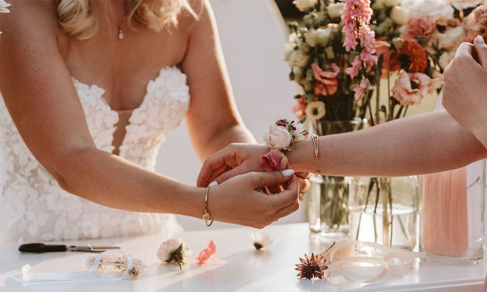 Nahaufnahme einer Braut, die einem Gast ein handgemachtes Blumenarmband anlegt.