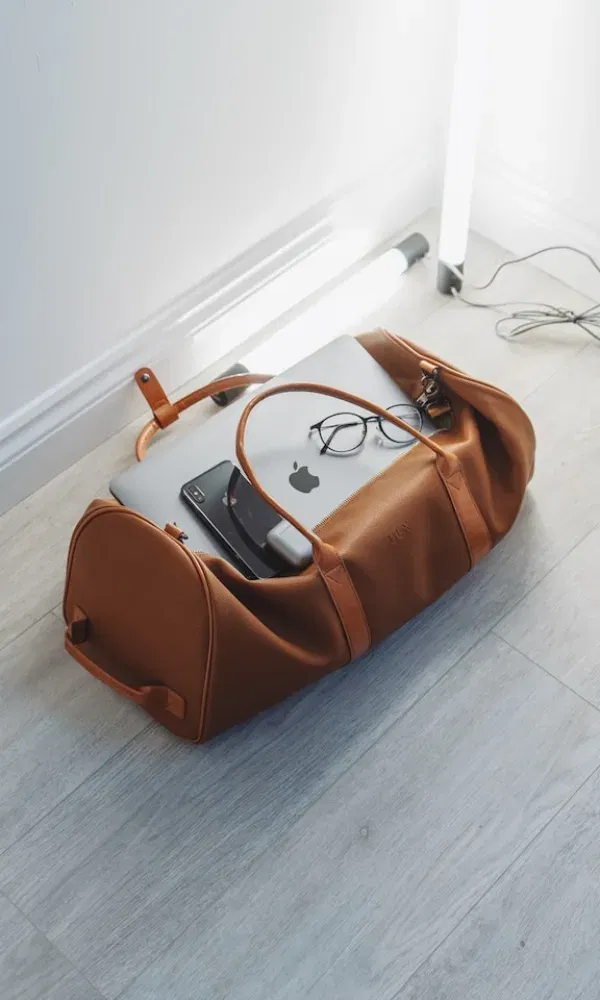 Moderne Ledertasche auf dem Boden mit Laptop, Handy, Brille und Kabel – ideal gepackt für den digitalen Nomaden.