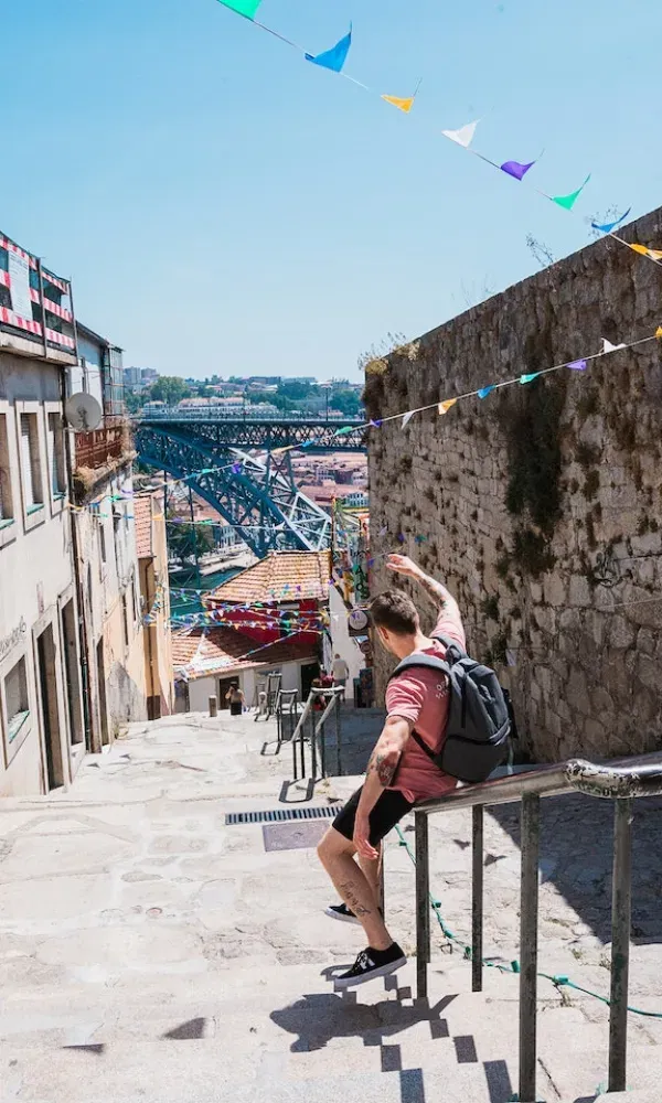 Szenische Straßenansicht mit Kopfsteinpflaster-Treppe in Porto: Ein junger Tourist rutscht auf dem Handlauf, bunte Fähnchen flattern im Wind.