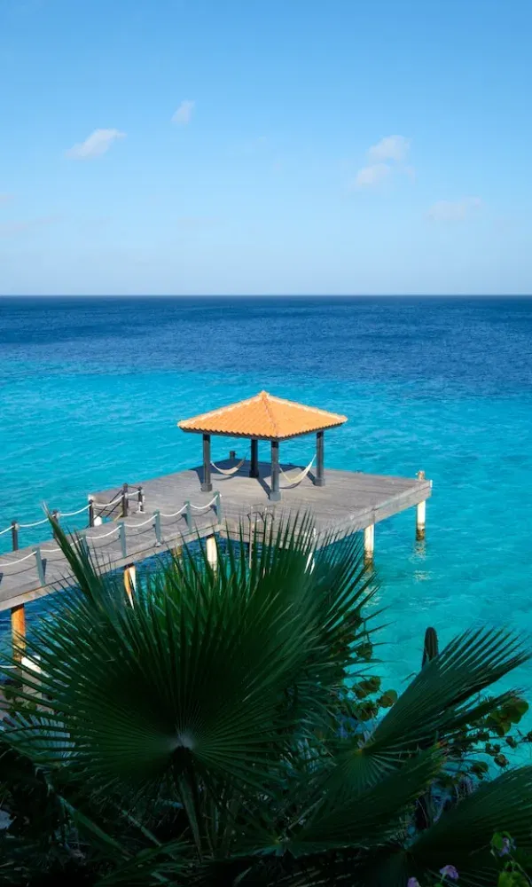 Traumhafte Aussicht auf einen über dem Meer erbauten Steg mit rotem Dach, umgeben von klarem Wasser und Palmen.