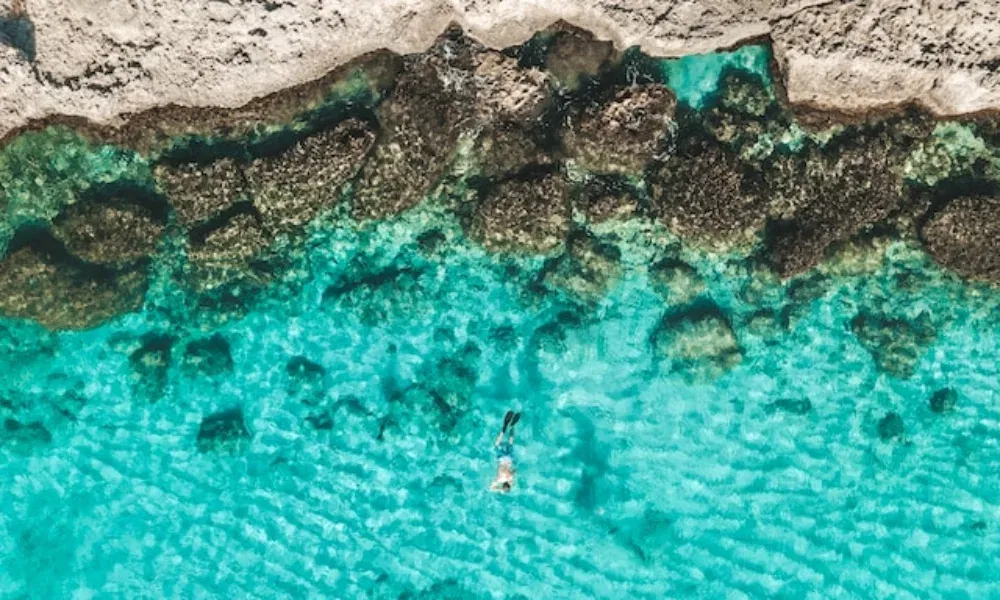 Von oben fotografierte Szene mit einer schnorchelnden Person über Korallen und Felsformationen im seichten Karibikmeer.