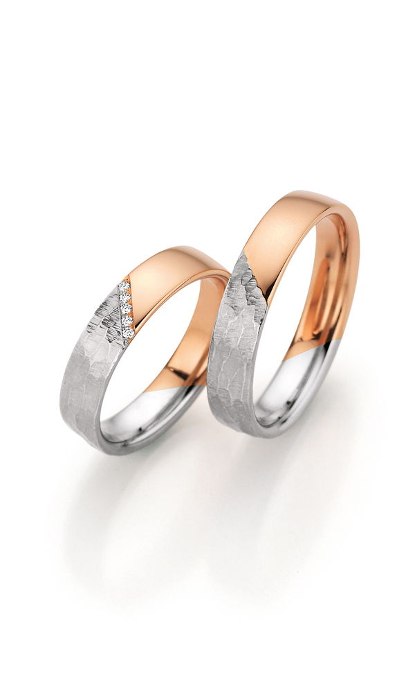 Elegante Trauringe aus warmem Roségold und strukturiertem Weißgold. Die kontrastreiche Oberfläche verleiht dem Design eine besondere Tiefe, während funkelnde Brillanten den Damenring schmücken.