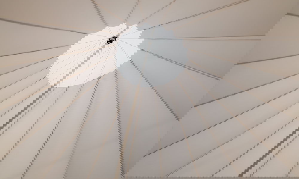 Symmetrischer Blickwinkel auf die spannweite eines weißen Sonnenschirms, der stilvollen Schatten für Outdoor-Feiern bietet.