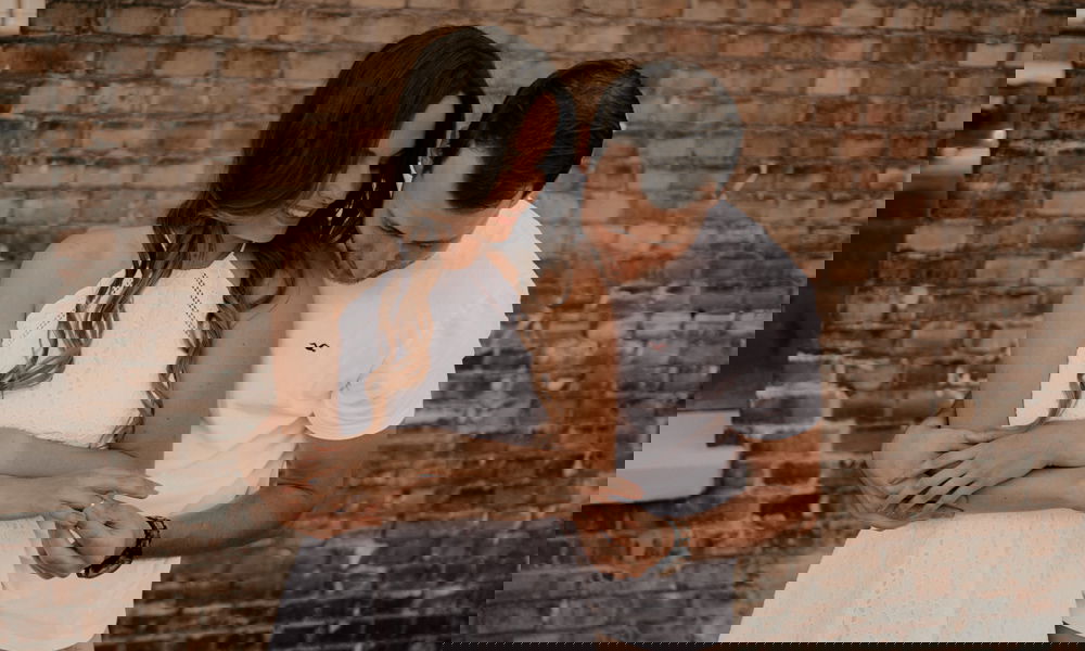 Romantischer Moment: Eine Frau im weißen Kleid wird von ihrem Partner umarmt, während beide ihren Verlobungsring bewundern.