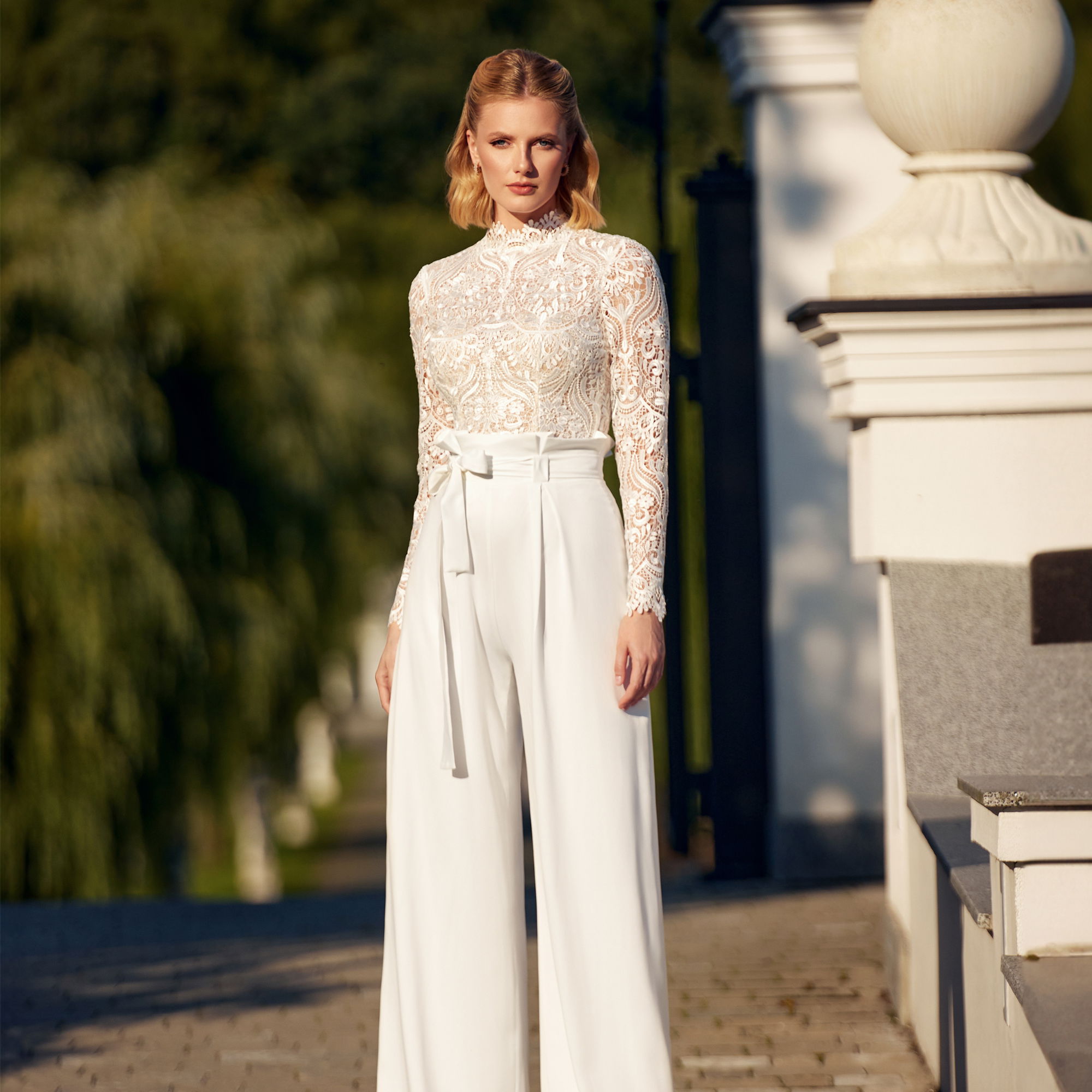 Stilvolles Braut-Ensemble mit hochgeschlossenem Spitzenoberteil und fließender Hose, ideal für eine zeitgemäße Hochzeit im Freien.