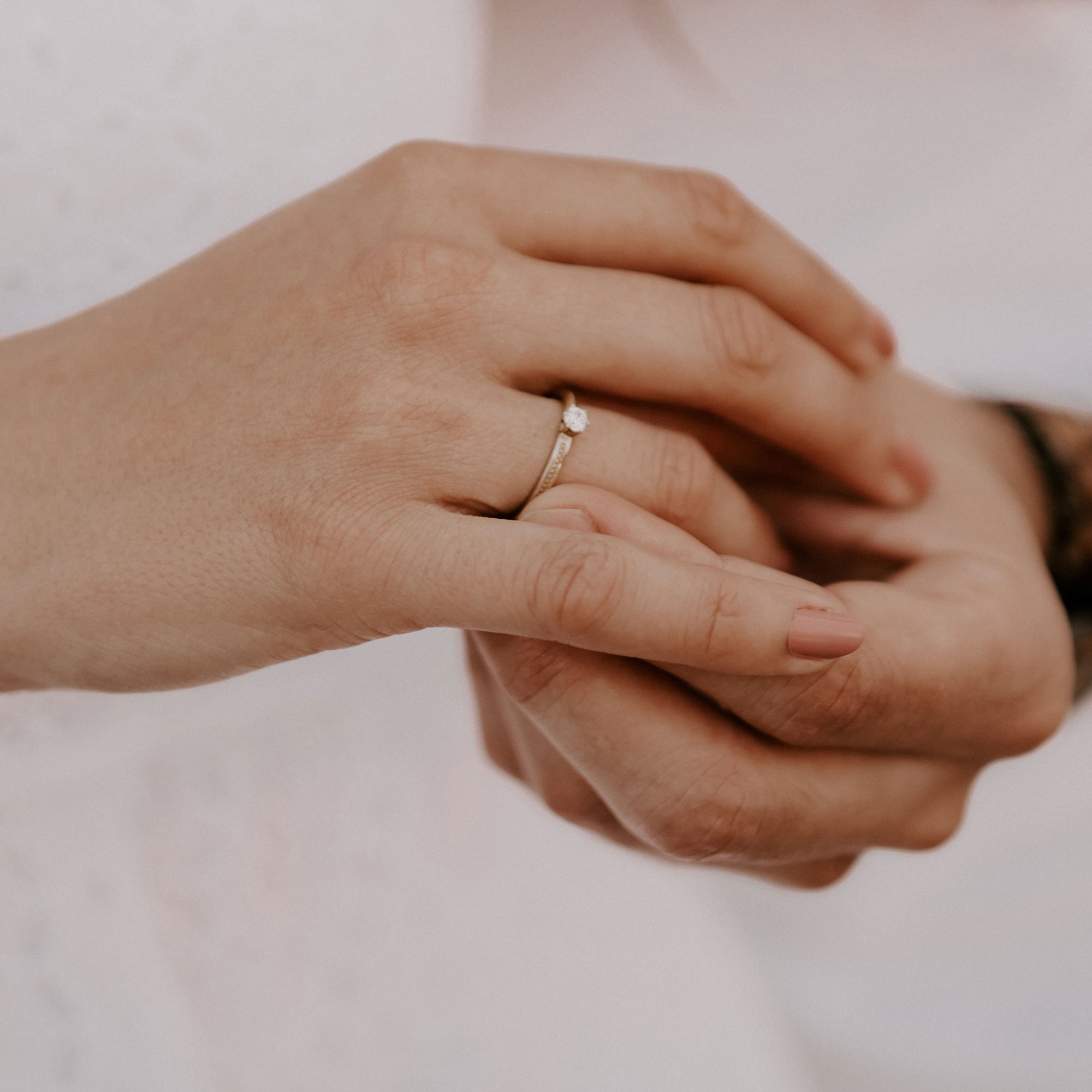 Verlobungsring aus Gold mit einem funkelnden Stein, getragen an der Hand einer Frau, zärtlich von einer anderen Hand gehalten.