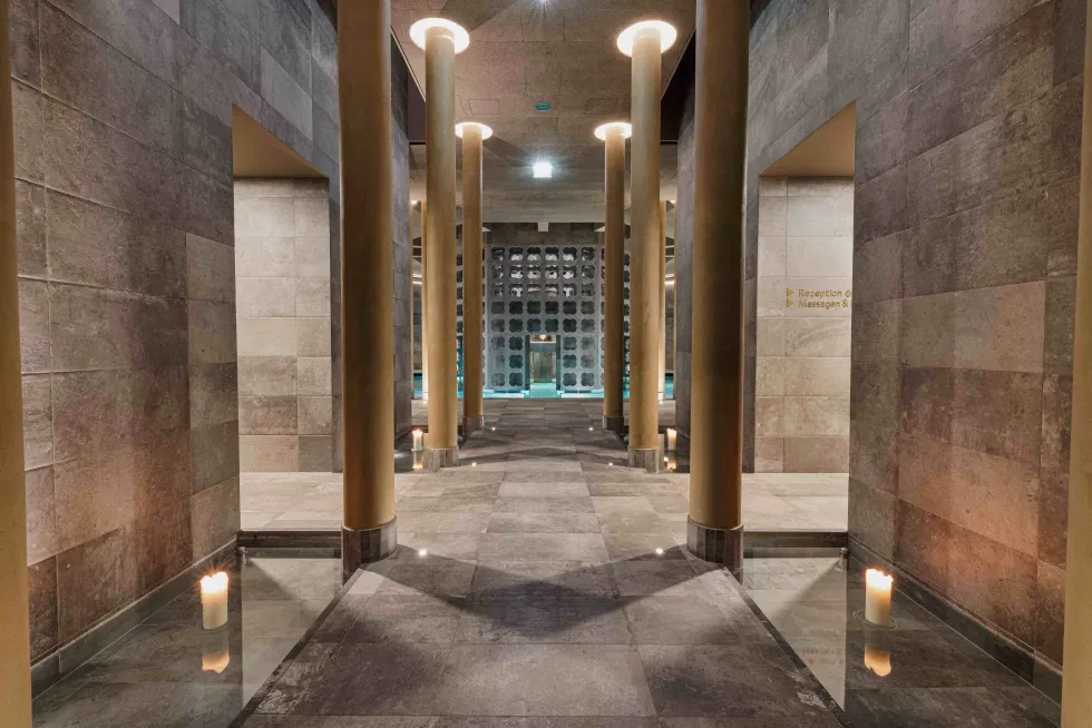 Moderner Spa-Bereich mit hohen Säulen, Steinwänden, Kerzen und Blick auf den Poolbereich im Hintergrund