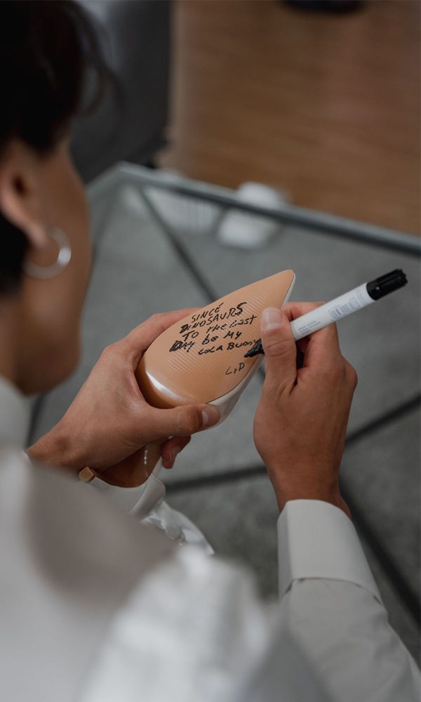 Nahaufnahme eines Mannes, der auf die Sohle eines Schuhs schreibt. Die handgeschriebene Botschaft wird mit einem Marker angebracht und verleiht den Hochzeitsschuhen eine persönliche Note.