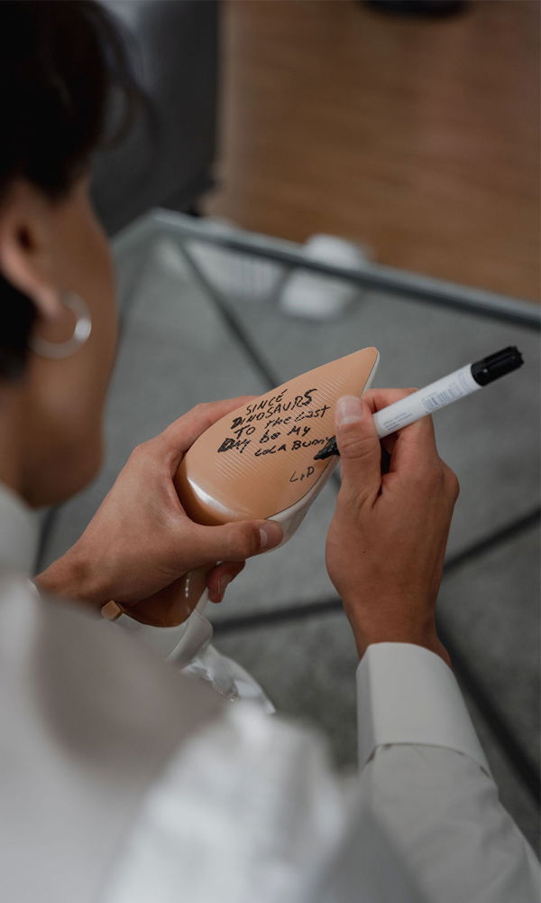 Nahaufnahme eines Mannes, der auf die Sohle eines Schuhs schreibt. Die handgeschriebene Botschaft wird mit einem Marker angebracht und verleiht den Hochzeitsschuhen eine persönliche Note.