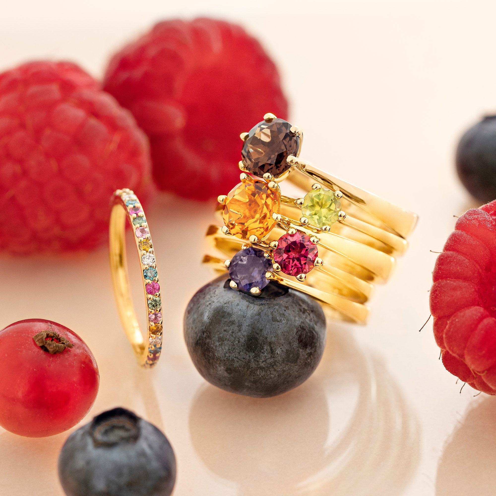 Farbige Edelsteine in Ringen auf einer stilvollen Komposition mit Himbeeren und Blaubeeren.