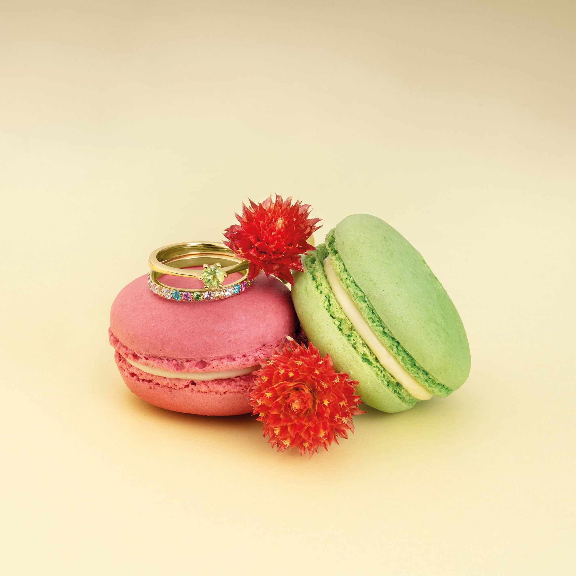 Farbige Edelsteine in Goldringen, elegant präsentiert mit Macarons und Blumen.