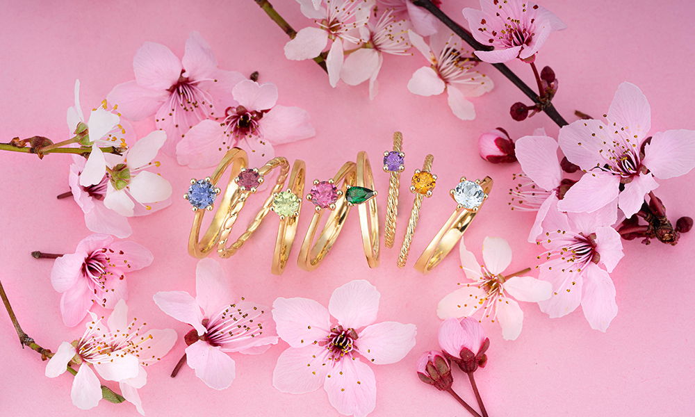 Farbige Edelsteine in goldenen Ringen, die zwischen Blüten der Kirschblüte präsentiert werden