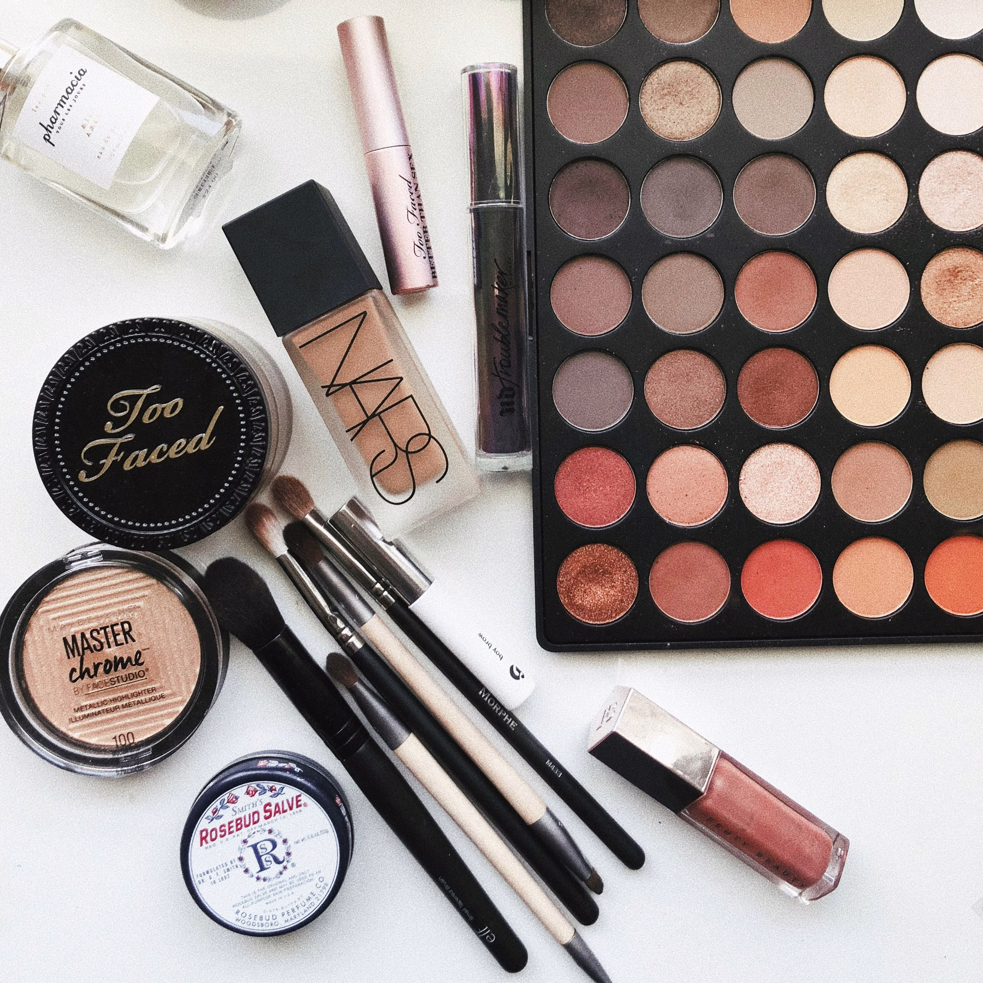 Eine Auswahl hochwertiger Kosmetik: Pinsel, Lidschatten in warmen Tönen, Highlighter und Lippenstift – Essentials für ein makelloses Brautstyling.