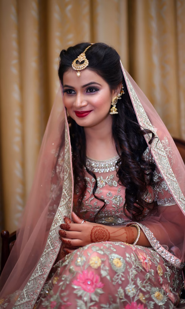 Eine lächelnde Braut in einem bestickten Hochzeitskleid und traditionellen Ornamenten, begleitet von kunstvollem Make-up und roten Lippen.