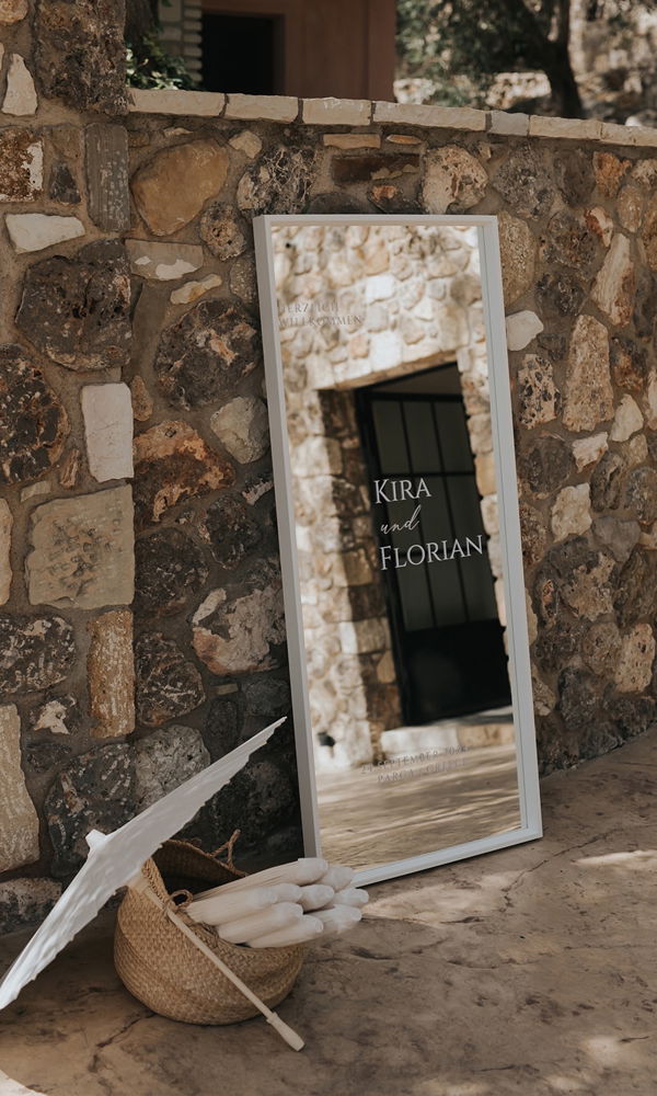 Hochzeitsschild mit reflektierendem Spiegelrahmen, umgeben von Naturstein und Sonnenschirmen – stilvolle Begrüßung für Gäste.