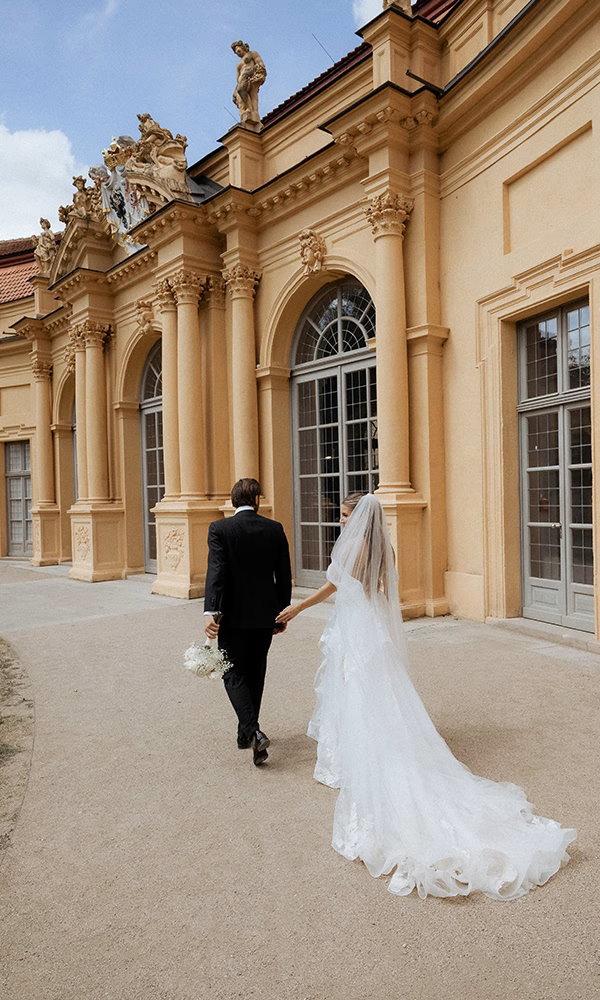 Rückansicht des Brautpaars auf dem Weg zu einer Hochzeit im Schloss-Ambiente.