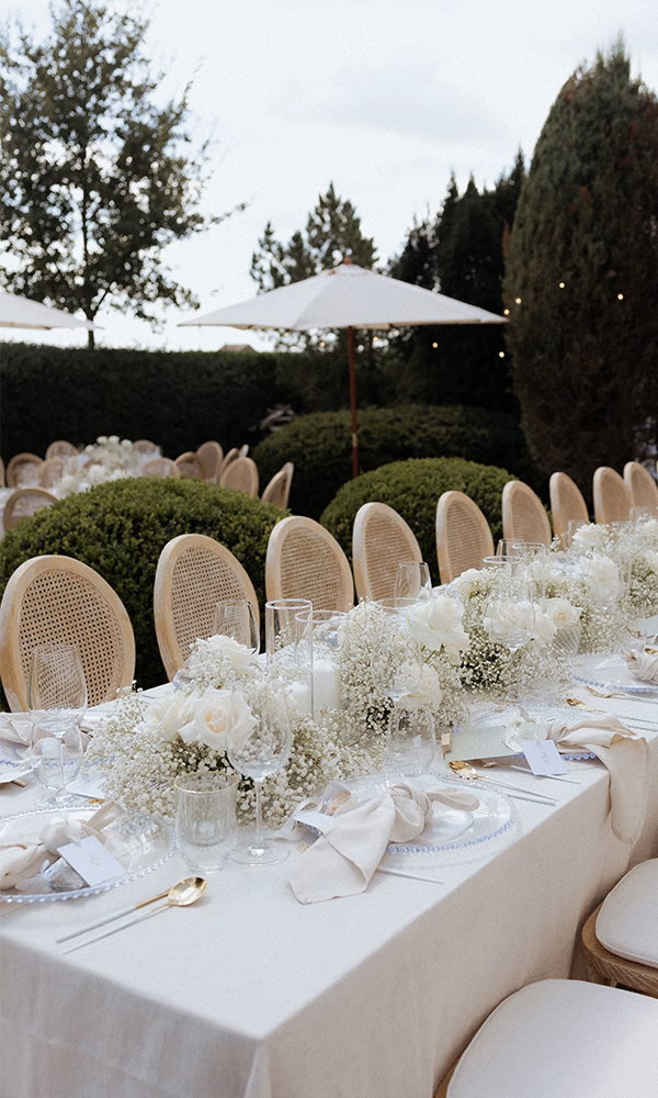 Outdoor-Hochzeitstisch mit Goldbesteck, Namenskarten und festlicher Dekoration.