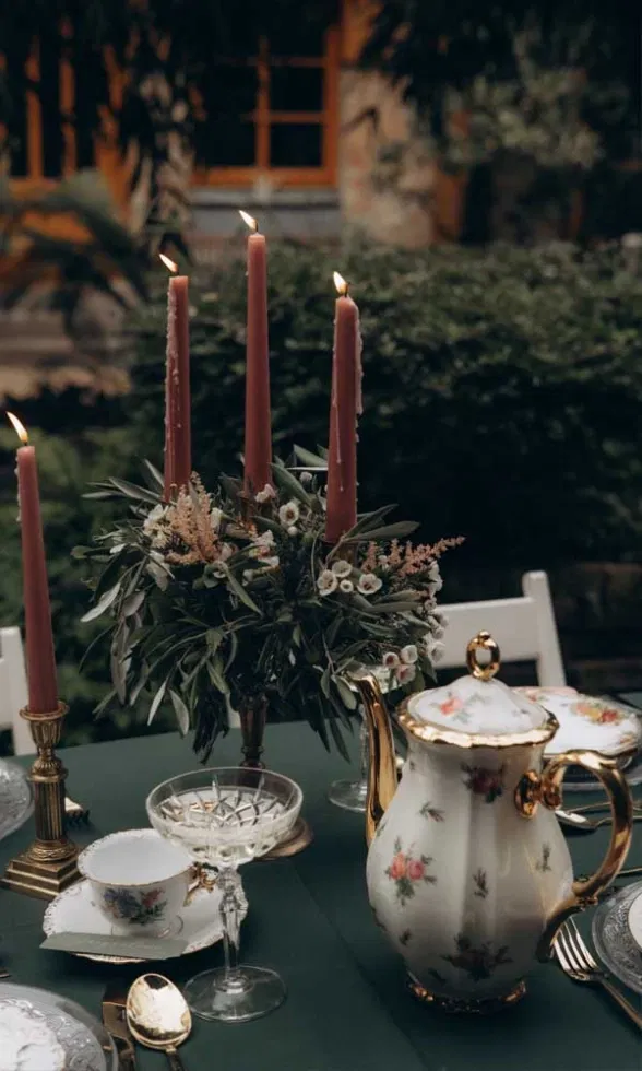 Stilvolle Hochzeits-Tischdekoration mit vintage Porzellan, floraler Teekanne und hohen Kerzen in warmen Erdtönen.