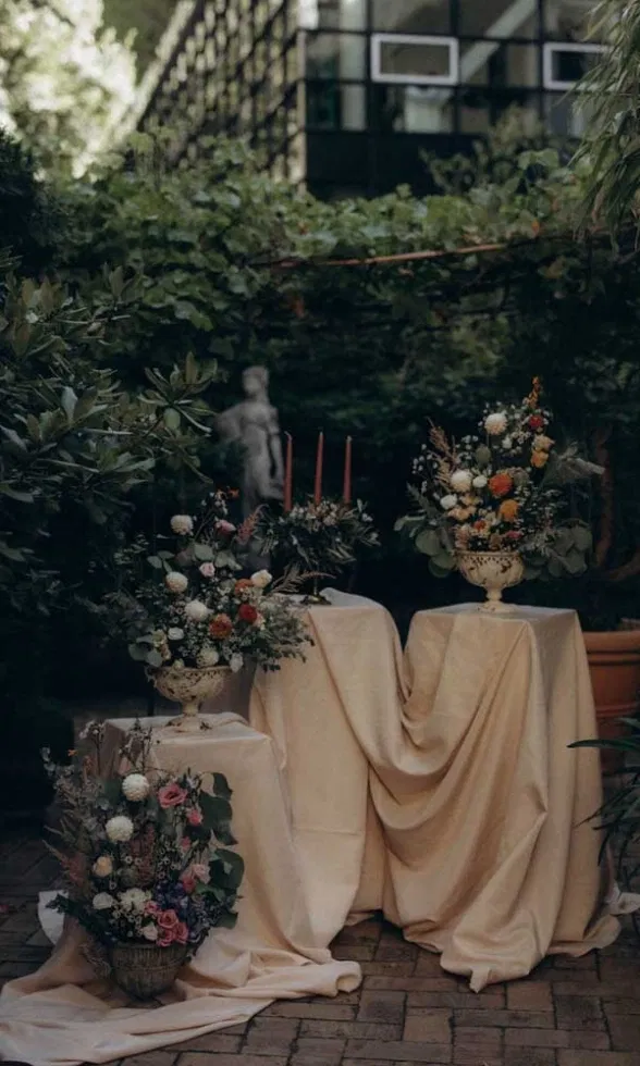 Romantische Hochzeitsdekoration im Urban-Garden-Stil mit floralen Arrangements, Kerzen und drapierten Stoffen im Grünen.