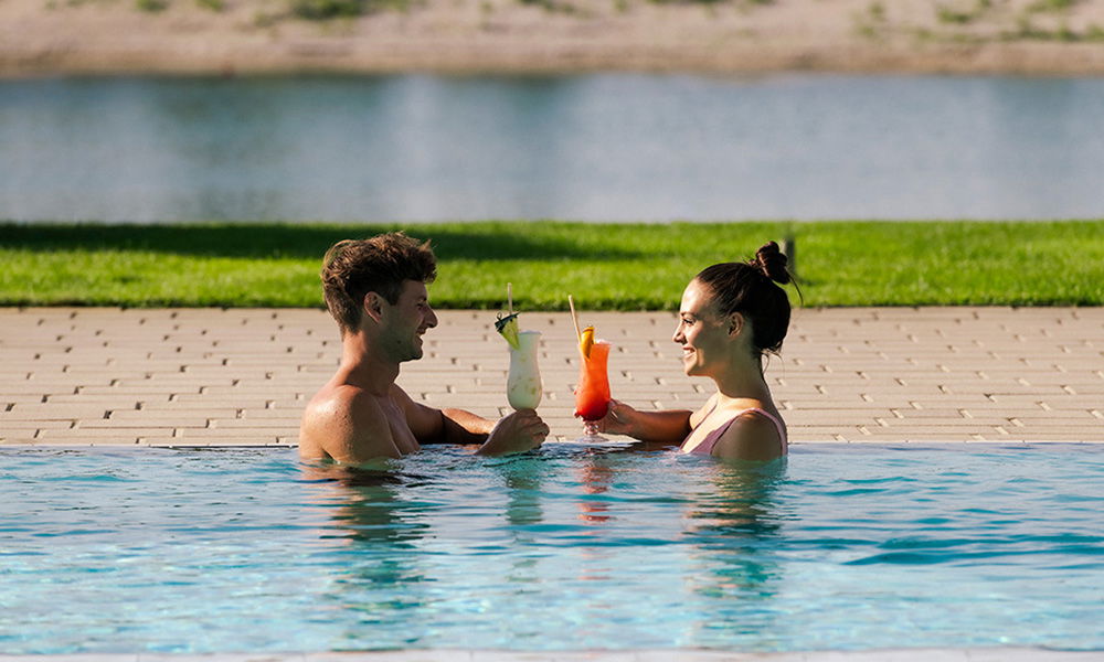 Paar genießt tropische Cocktails im Pool mit Blick auf den See.