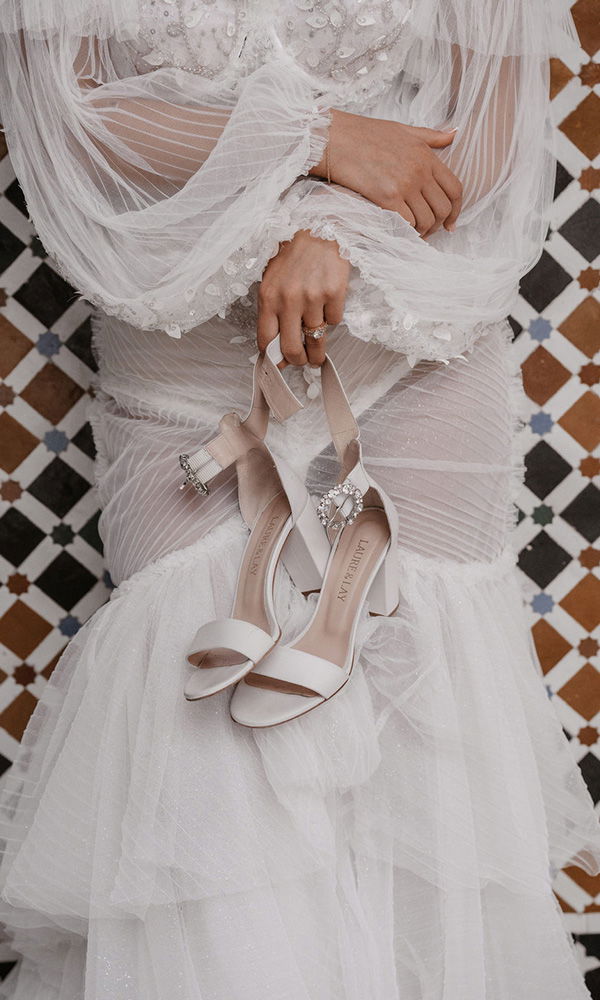 Nahaufnahme einer Braut, die elegante High Heels in der Hand trägt.