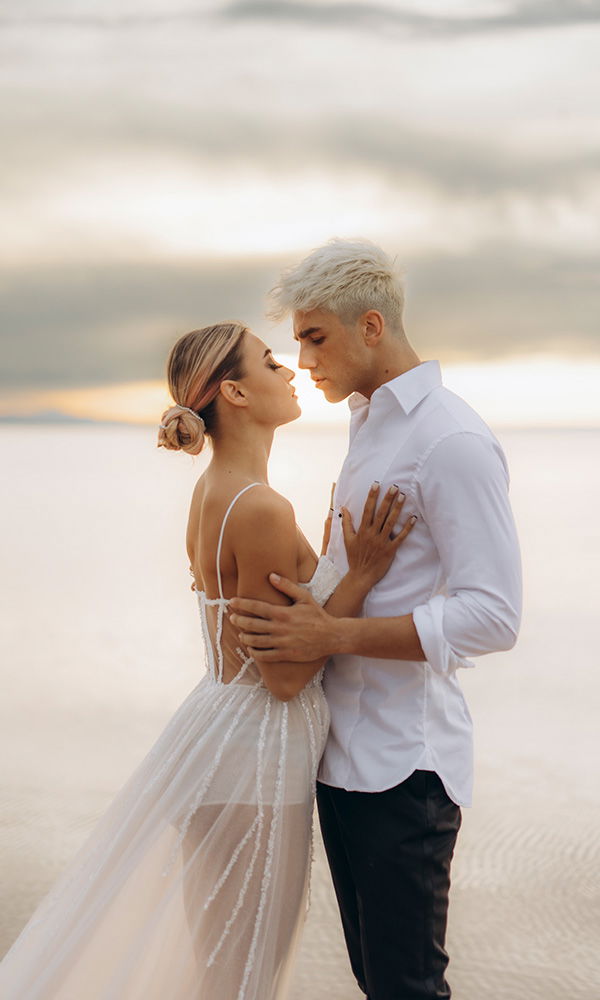 Hochzeitspaar umarmt sich am Wasser im goldenen Abendlicht.