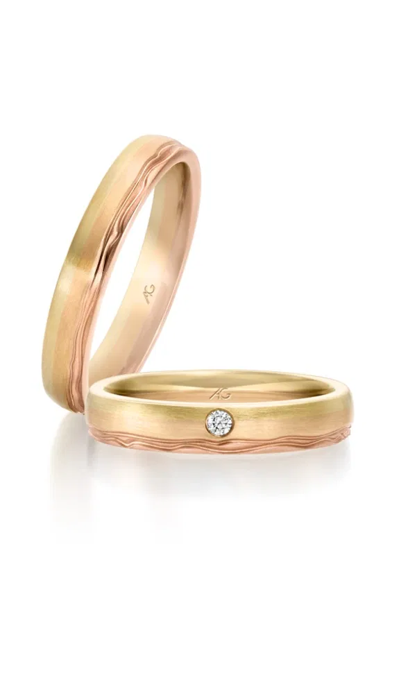 Zwei bicolor Trauringe aus Gelb- und Roségold mit matter Oberfläche, feiner Wellenstruktur und einem dezent eingefassten Diamanten.