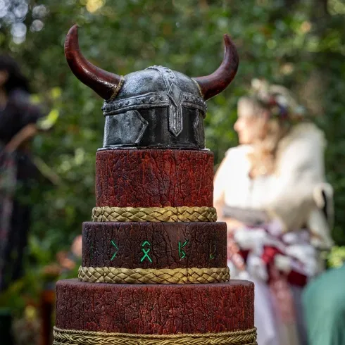 Wikinger Hochzeitstorte mit rustikaler Holzoptik, goldenen Flechtdetails und Wikingerhelm als Tortenaufsatz im Wald
