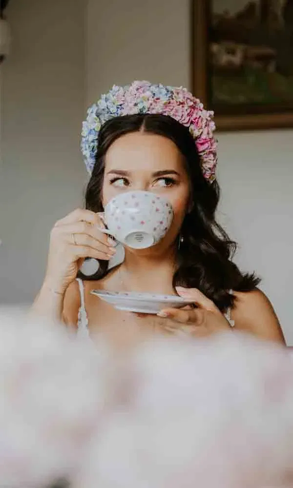 Junge Frau mit dunklem Haar genießt Tee, trägt einen pastellfarbenen Blumenkranz.