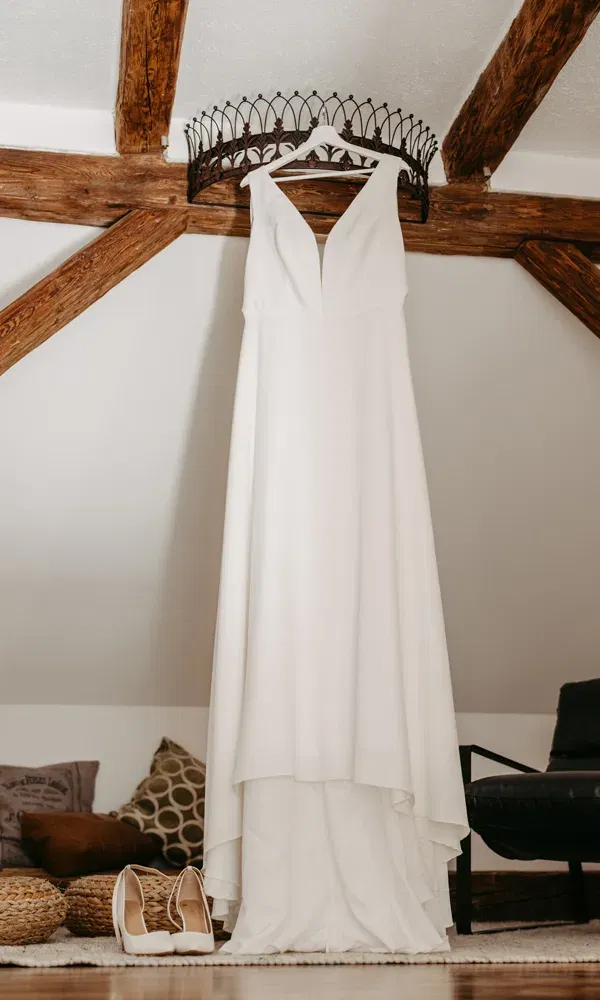 Ein modernes Brautkleid mit V-Ausschnitt und fließendem Rock hängt dekorativ im gemütlichen Dachzimmer.