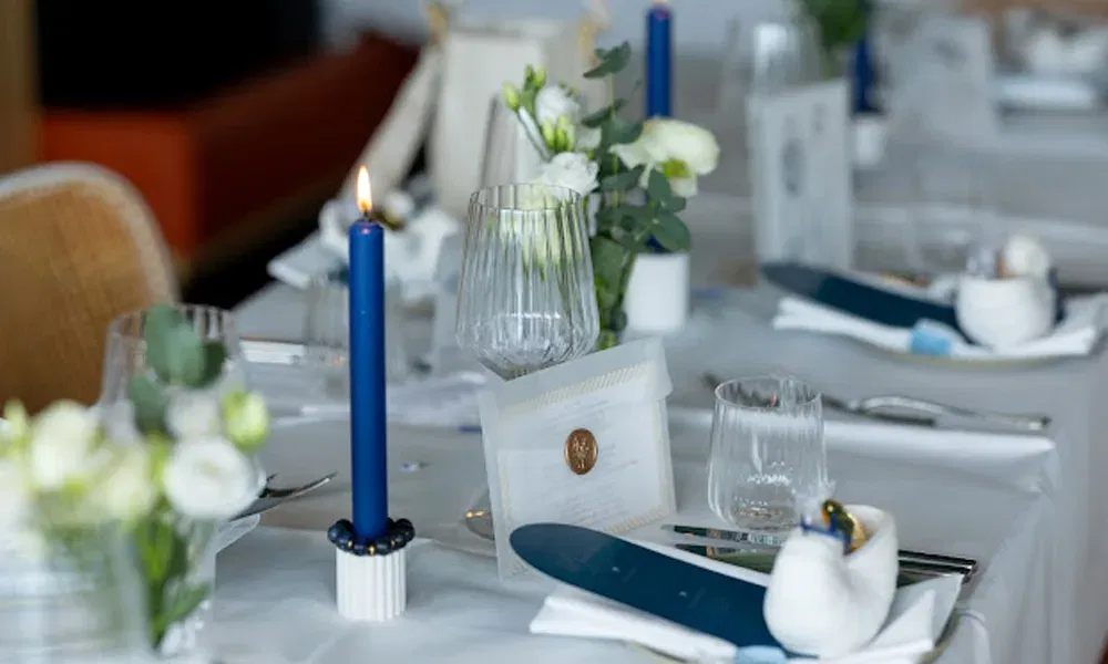 Detailaufnahme einer stilvollen Hochzeitstafel mit blauer Kerzendeko, Glaswaren, Eukalyptus und fein gestalteter Papeterie.