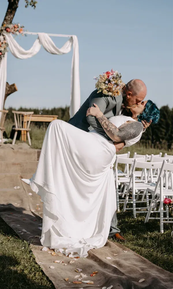 Braut und Bräutigam küssen sich innig nach dem Jawort unter freiem Himmel, eingerahmt vom Traubogen und leeren Stuhlreihen.
