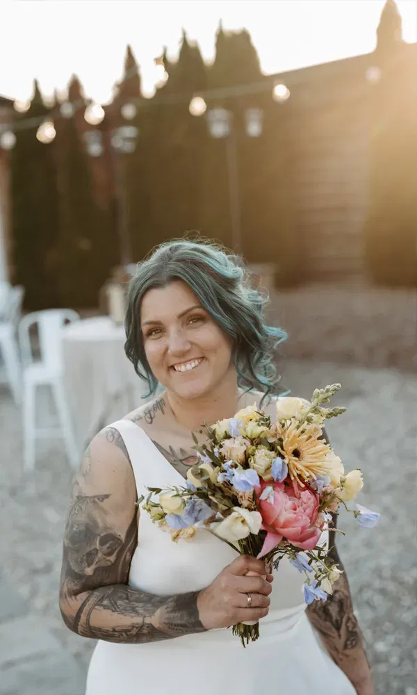 Rebeka mit blauen Haaren und tätowierten Armen präsentiert ihren Strauß aus Pfingstrosen, Ranunkeln und Wildblumen.