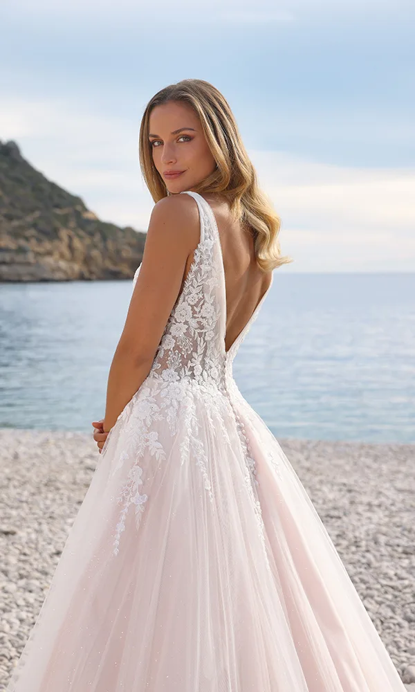 Brautkleid mit tiefem Rückenausschnitt und floraler Spitze, das mit einem fließenden Rock in Blushton für einen traumhaften Auftritt am Strand sorgt.