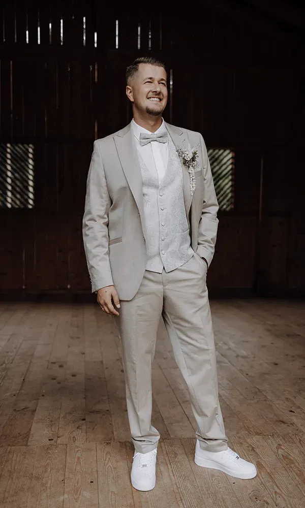 Moderner Bräutigam im beigen Anzug mit weißen Sneakers und floraler Ansteckblume.