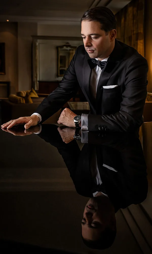 Edles Porträt eines Bräutigams im schwarzen Smoking mit Reflexion auf Hochglanzfläche.