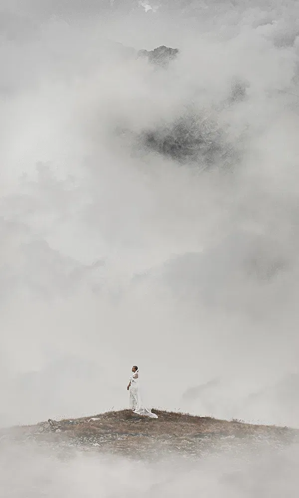 Mystische Aufnahme einer Braut im weißen Kleid auf nebliger Bergspitze.