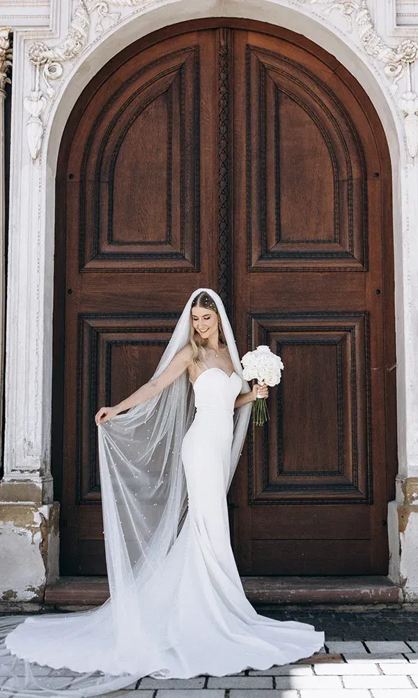 Klassische Braut mit langem Schleier vor antikem Holztor.