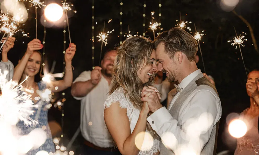 Brautpaar tanzt eng umschlungen im Schein von Wunderkerzen bei Nacht.