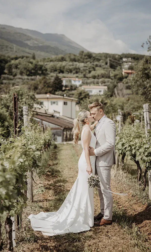 Brautpaar küsst sich innig zwischen Reben im sonnigen Weinberg.