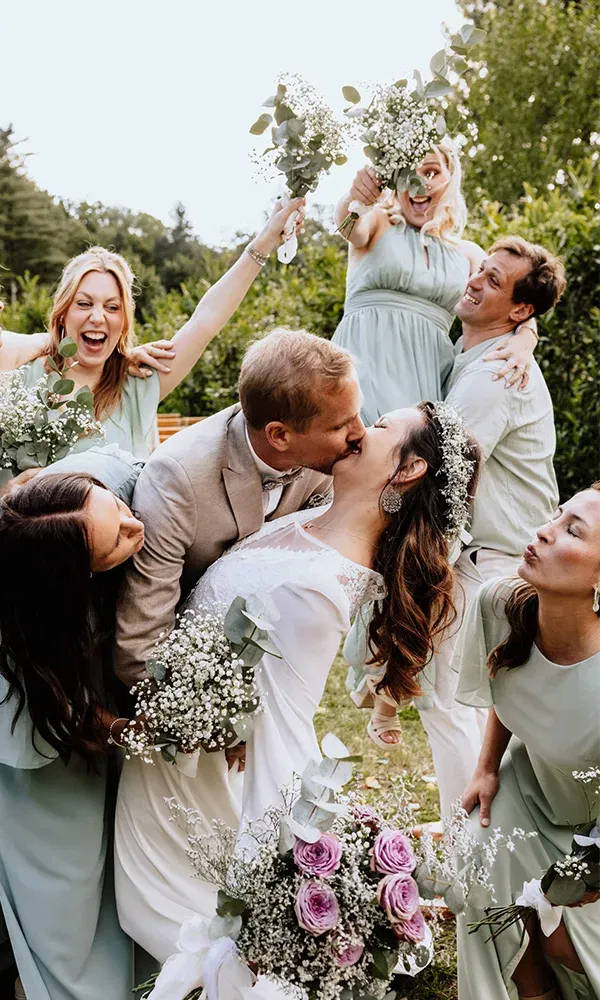 Kuss des Brautpaares umgeben von fröhlichen Trauzeugen.