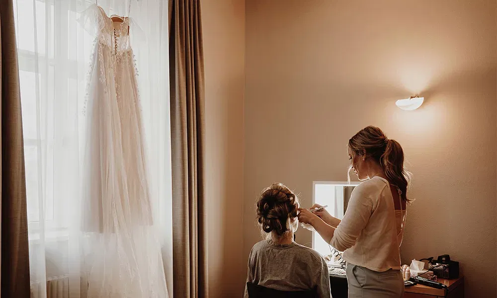 Getting-Ready-Moment mit Stylistin, während das Brautkleid bereit hängt.