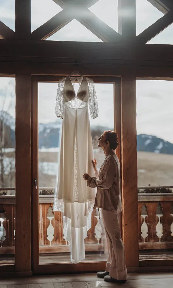 Braut bewundert ihr Kleid im Morgenlicht vor alpiner Kulisse.