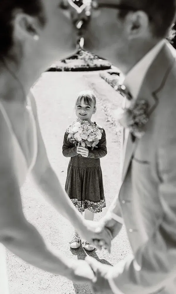 Brautpaar küsst sich, während ein Mädchen mit Blumenstrauß zwischen ihnen steht und lächelt.