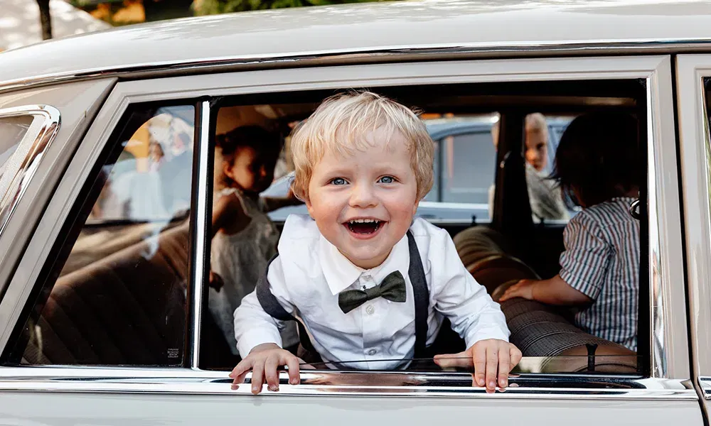 Junge schaut mit leuchtenden Augen aus dem Autofenster und lacht in die Kamera.