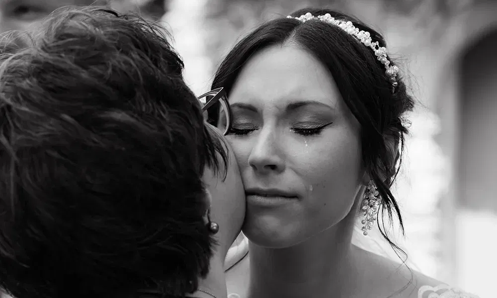 Eine emotionale Braut schließt die Augen, während eine Frau ihr einen Kuss auf die Wange gibt.