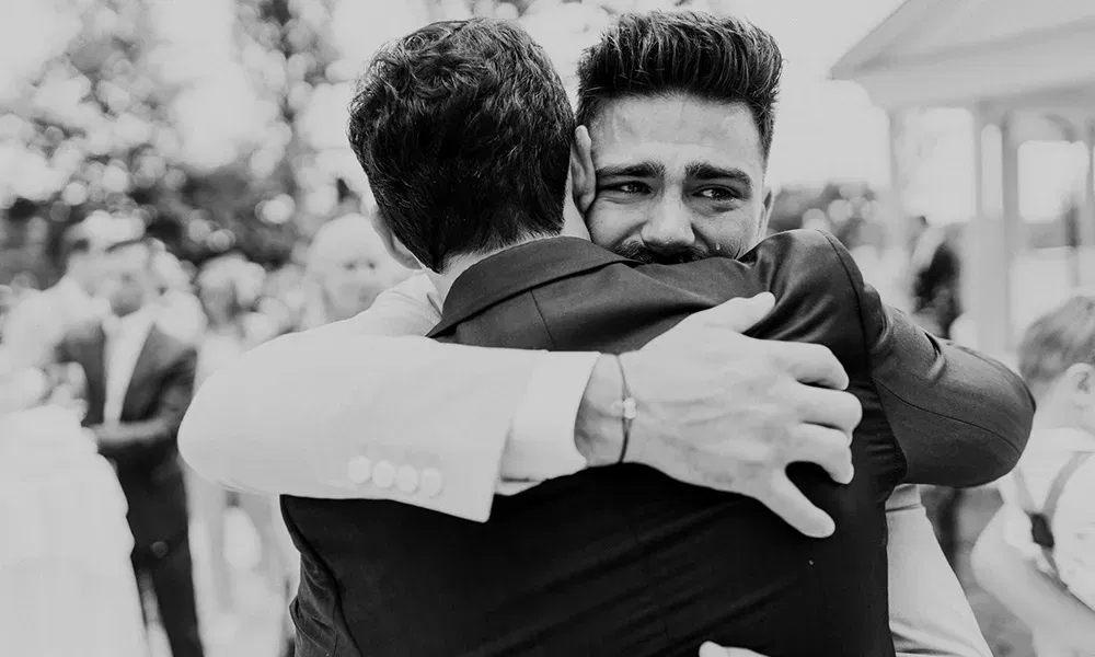 Zwei Männer umarmen sich intensiv, einer davon mit Tränen in den Augen.