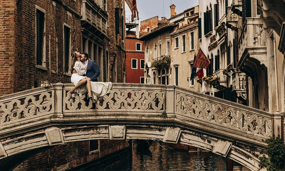 Romantischer Kuss auf Brücke in Venedig – Brautpaar zwischen historischen Fassaden.