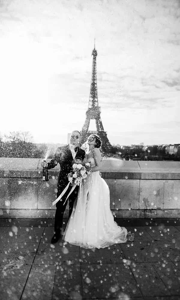 Brautpaar stößt mit Champagner vor dem Eiffelturm an, umgeben von funkelnden Tropfen.