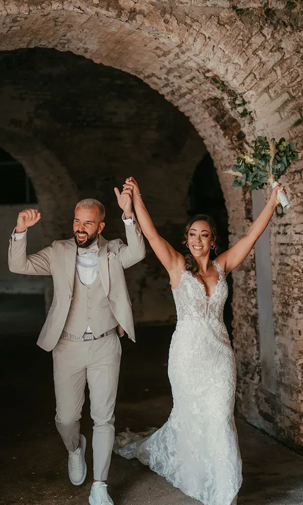 Frisch verheiratetes Paar verlässt strahlend die Zeremonie und jubelt mit erhobenen Armen.